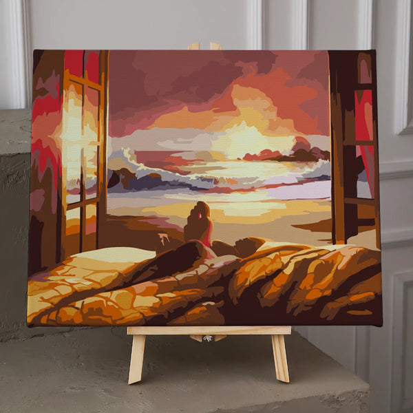 Person watching sunset over ocean from cozy bed near window