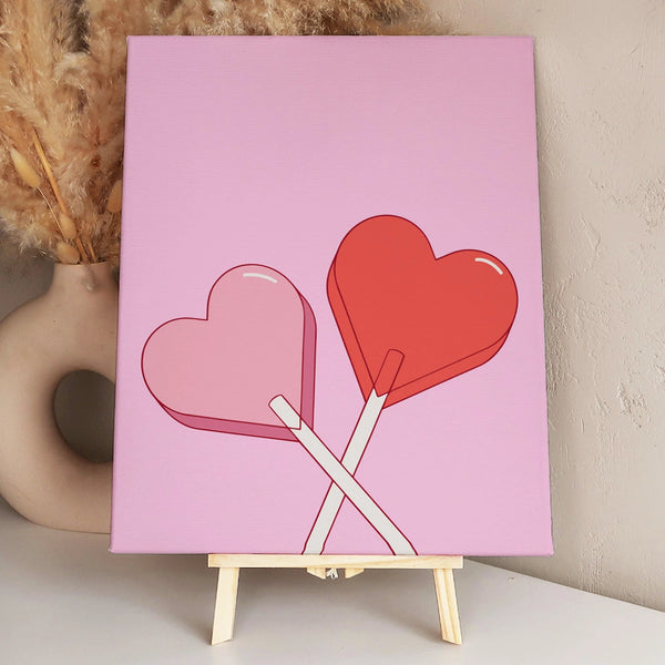 Two heart-shaped lollipops crossed against a pink background.