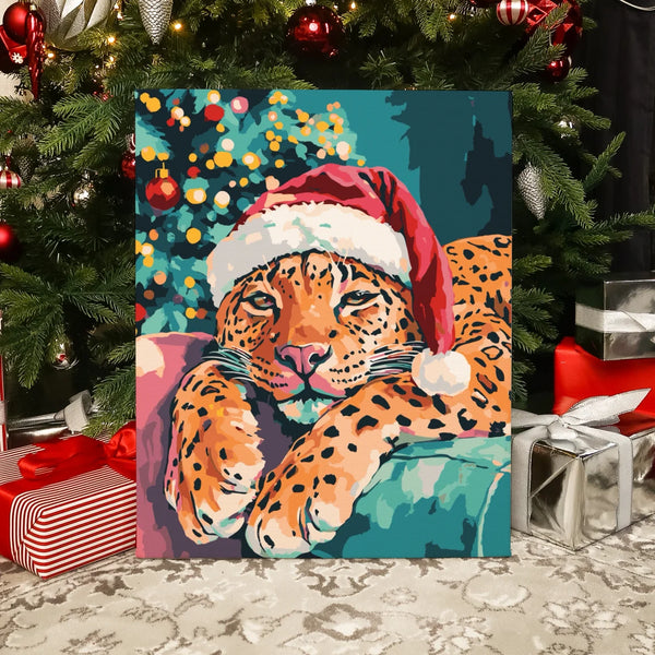 Completed Christmas Paws paint by numbers artwork showing a relaxed leopard in a Santa hat beside a glowing Christmas tree.
